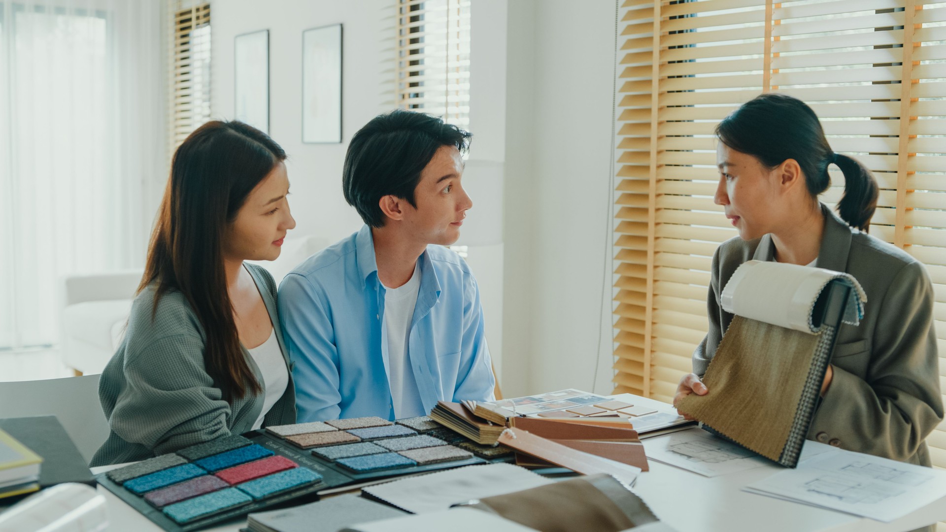 Asian tenants choose colors, patterns, and materials and give them to female interior designer for new house. Happy couple buy real estate for investment.